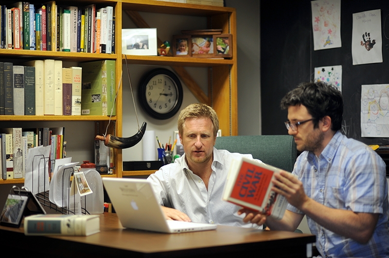 Two men discussing history research in an office
